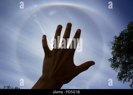 Stockholm, Sweden - August 6 2018: Circular rainbow around the sun which is blocked by the hand of a young male - with a wedding ring on it. Meteorolo Stock Photo