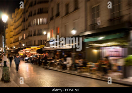 Blurry motion image of people walking on street passing by cafes and bistros at night in Paris. Stock Photo