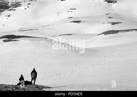 Two hikers on halt in snowy mountain. Black and white toned landscape. Stock Photo