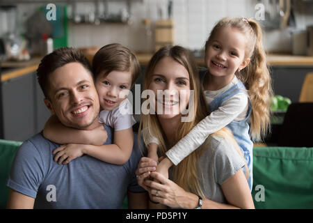 Happy parents piggybacking son and daughter sitting on sofa, por Stock Photo