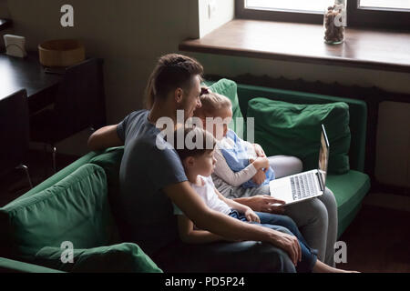Family with children watching video on laptop together on sofa Stock Photo