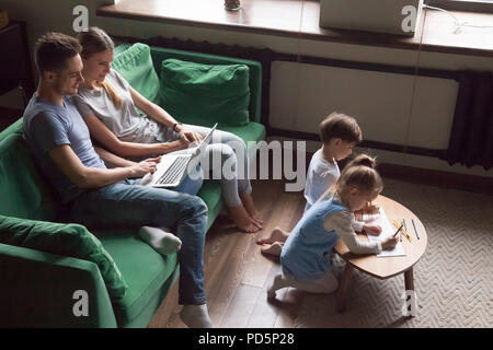 Kids siblings drawing together while parents using laptop at hom Stock Photo