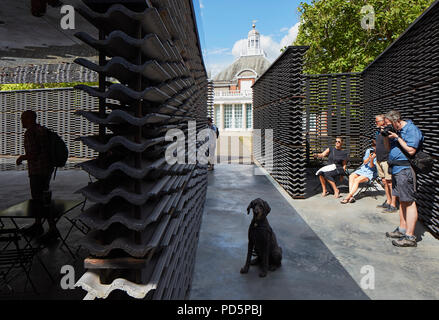 Inside pavilion looking to Serpentine Gallery with people and dog. Serpentine Summer Pavilion 2018, London, United Kingdom. Architect: Frida Escobedo, Stock Photo