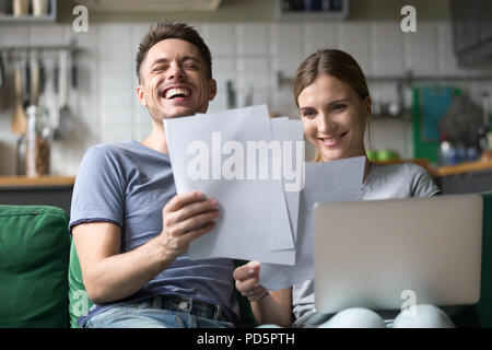 Happy couple laughing having fun with documents and laptop Stock Photo