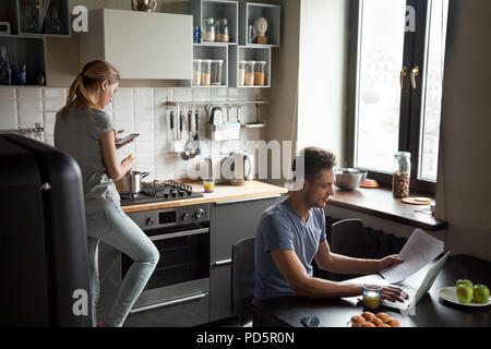 Young couple using laptop and smartphone in the kitchen Stock Photo