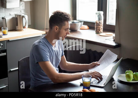 Young man working with laptop while having breakfast at home Stock Photo