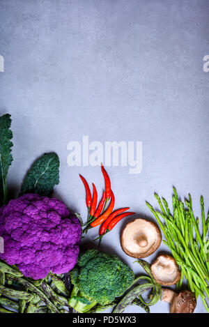 Healthy vegetarian cooking ingredients, colorful vegetables on concrete table, purple cauliflower, chilli, mushrooms, asparagus, broccoli. Stock Photo