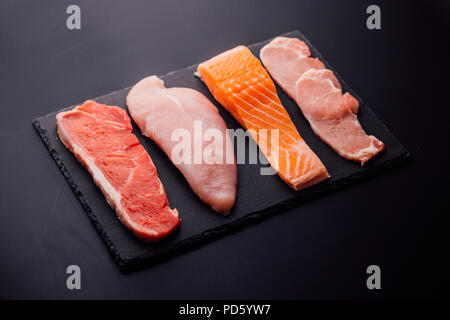 Group of animal proteins, chicken, meat, fish and pork on a black background Stock Photo