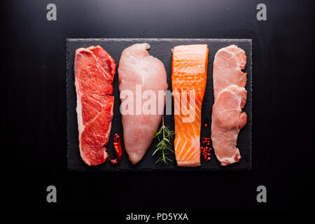 Group of animal proteins, chicken, meat, fish and pork on a black background Stock Photo