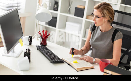 A young girl is sitting at a table in the office, holding a yellow marker in her hand. Before the girl lies an open book. Stock Photo