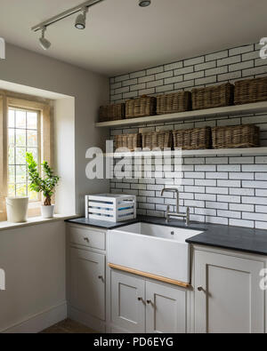 Wicker baskets on shelving above Butler sink in tiled utility room. Stock Photo