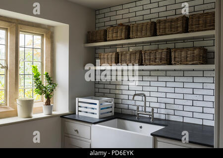Wicker baskets on shelving above Butler sink in tiled utility room. Stock Photo