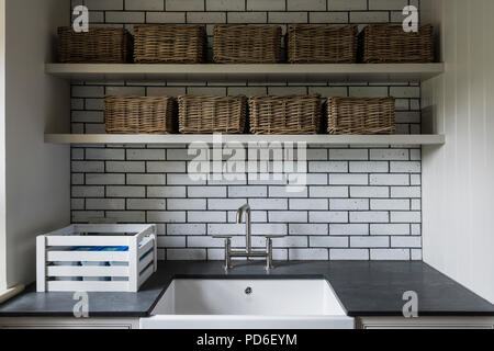 Wicker baskets on shelving above Butler sink in tiled utility room. Stock Photo