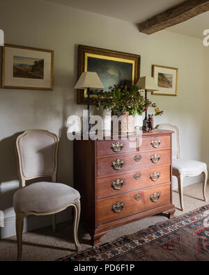 Wooden vintage chest of drawers with framed artwork and chairs Stock Photo