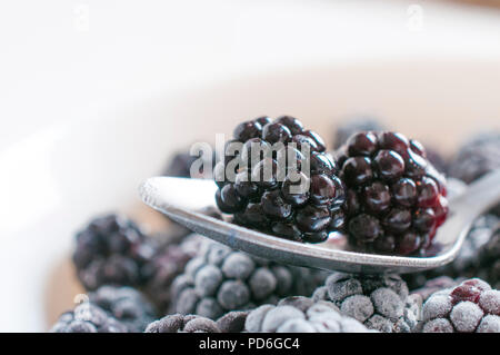 Fresh blackberries on a spoon over some frozen blackberries Stock Photo