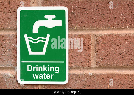 Drinking water sign with white text and tap faucet symbol and glass symbol on green background on red brick wall. Environmental water issues concept Stock Photo