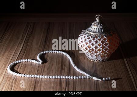 A golden light Ramadhan candle with Islamic white rosary beads on dark background, wood table Stock Photo
