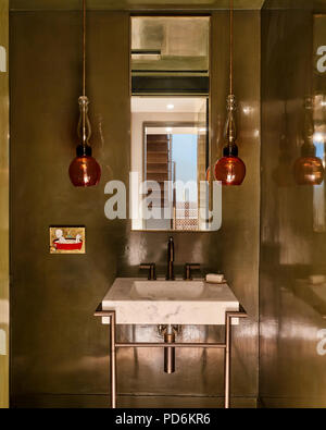 Coloured glass pendant shades with mirror above marble sink. Stock Photo