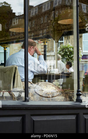 Businessman in shirt sitting at table, having breakfast at Betty's café, Harrogate seen through the window. Stock Photo