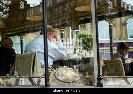 Businessman in shirt sitting at table, having breakfast at Betty's café, Harrogate seen through the window. Stock Photo