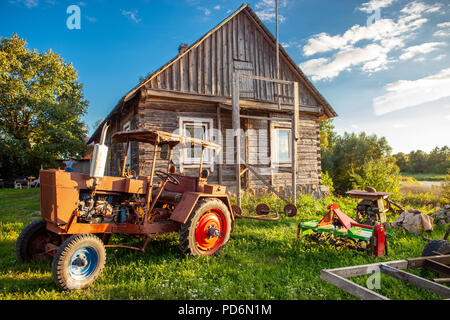 Typical Lithuanian wooden house with old tractor in the countryside on a summer evening Stock Photo