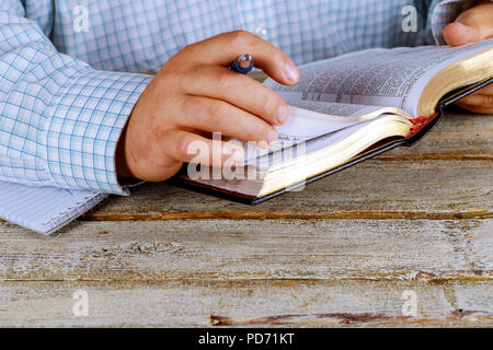 Man is holding a pen in his hand with an open book Holy Bible lying in fornt of him Stock Photo