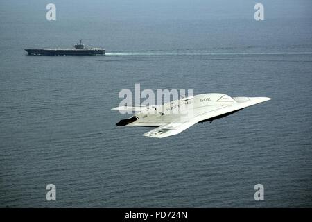 An X-47B Unmanned Combat Air System demonstrator flies near the aircraft carrier USS George H.W. Bush. Stock Photo