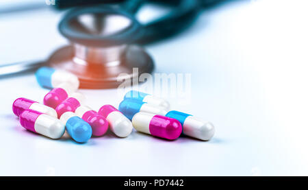 Green stethoscope with pile of antibiotic capsule pills on white table near drug tray. Antimicrobial drug resistance and overuse. Medical equipment fo Stock Photo