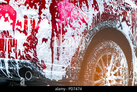 Red compact SUV car with sport and modern design washing with soap. Car covered with white foam. Car care service business concept. Car wash with foam Stock Photo