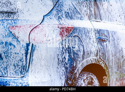 Blue compact SUV car with sport and modern design washing with soap. Car covered with white foam. Car care service business concept. Car wash with foa Stock Photo