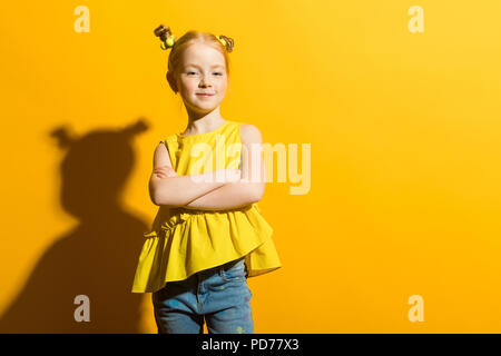 Girl with red hair on a yellow background. The beautiful girl folded her arms across her chest. Stock Photo