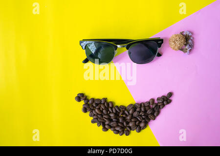top view flat layer funny face made from coffee beans in smile  icon shape , wooden grinder basket and sun glasses on two tone multicoloured  backgrou Stock Photo