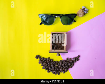 top view flat layer funny face made from coffee beans in smile  icon shape , wooden grinder basket and sun glasses on two tone multicoloured  backgrou Stock Photo