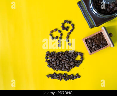 top view flat layer coffee beans in cup and smell icon shape and vintage wooden coffee grinder on yellow background Stock Photo