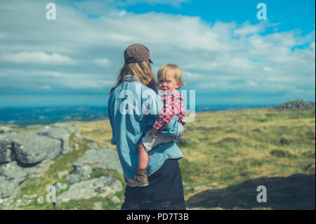 A young mother and her little toddler are admiring the view from the top of a rock on a hill in the moor Stock Photo