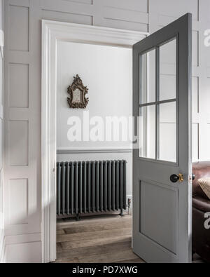 View through open door to hall with Neo-classic model radiator from Arroll. A 1750's gilt framed mirror hangs above the radiator. Stock Photo