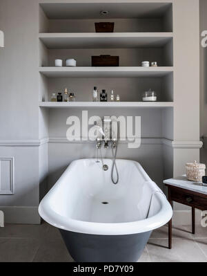 Free-standing roll top bath from Albion in bathroom with antique marble topped table and inbuilt shelving. The outside of the bath is painted in Raili Stock Photo