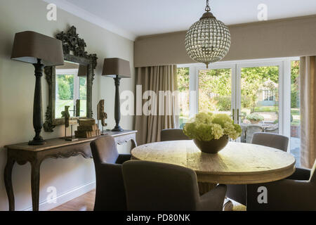 Round crystal-effect chandelier by Artisanti above round wooden dining table Stock Photo