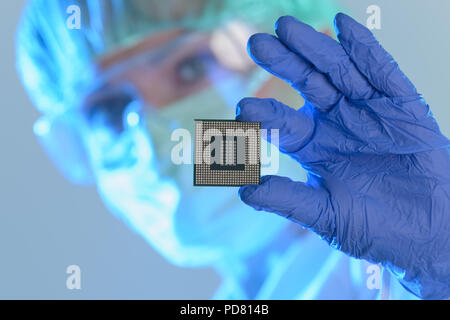 An engineer working in a laboratory wearing a special uniform and protective gloves holds new processor in hands and examines it Stock Photo