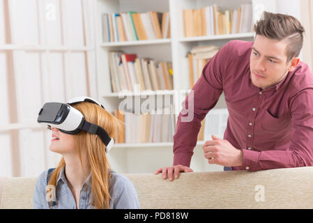 Young woman using virtual reality headset and her boyfriend or partner upset about this situation Stock Photo