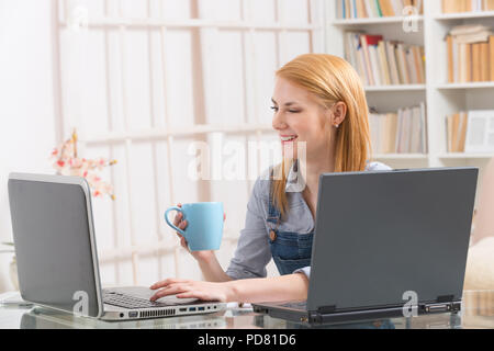 Young woman sitting at table and working with two laptops at home Stock Photo