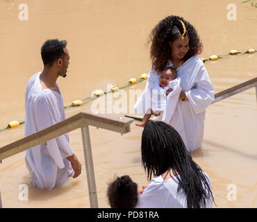 River Jordan, Israel  May 19  2018:  Ethiopian Christian pilgrim family with a baby, dressed in white,  being baptised at the same place in the brown  Stock Photo