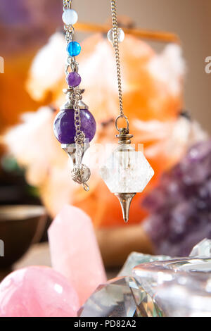Pendulums crystal pendulum, amethyst, tool for dowsing. Crystals undrneath an in backbround. Stock Photo