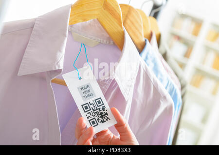 Woman's hand with a cloth label with QR code  in a shop Stock Photo