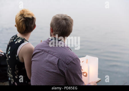 Seattle, Washington: A young couple with paper lanterns watch the ceremony at the From Hiroshima To Hope gathering at Green Lake Park. The ceremony is held in remembrance of atomic bomb victims on the anniversary of the bombing of Hiroshima, Japan. The annual lantern floating ceremony honors victims of the bombings of Hiroshima and Nagasaki, and all victims of violence.  The ceremony is an adaptation of an ancient Japanese Buddhist ritual, the Toro Nagashi, in which lante Credit: Paul Christian Gordon/Alamy Live News Stock Photo