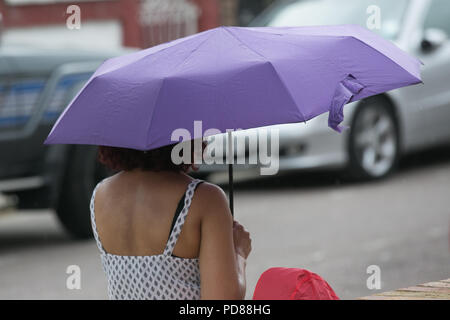 London. UK - A woman shelters from the rain beneath an umbrella rain starts to fall in north London. The Met Office has issued a weather warming with thunderstorms likely across the London and South East of England from 4pm today until 3am tomorrow morning (Wednesday) after couple months of the heatwave.  Credit: Dinendra Haria/Alamy Live News Stock Photo