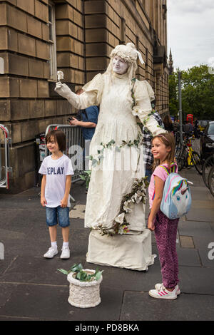 Edinburgh, Scotland, UK. 7th August 2018. One woman performs as a living statue, interacting and posing with two young children. Street acts and artists, alongside promoters of Fringe Festival events, ply the streets of Edinburgh Festival, providing entertainment and amusement to the many visitors to the Fringe. Credit Joseph Clemson, JY News Images/Alamy Live News. Stock Photo