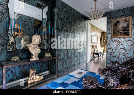 Carved armchairs with bust and blue candles on console in entrance hall, silvered embossed wallpaper by Cole & Sons Stock Photo