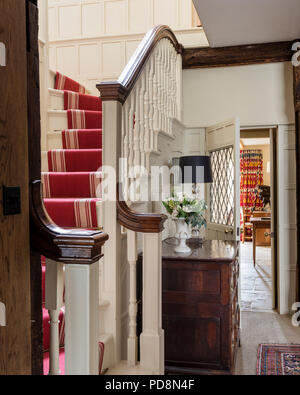 Wood panelled entrance hall with red carpet runner, 18th century oak wood chest and modern lamp Stock Photo