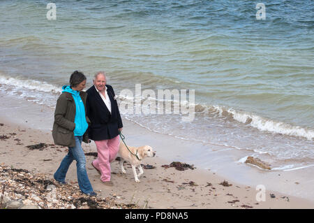 Middle aged mixed gender couple walking with yellow labrador dog along the beach and coast at Fort Victoria, Isle of Wight, UK Stock Photo